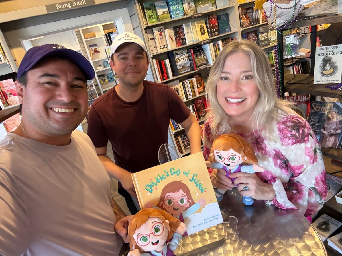 Three smiling adults with children's book and dolls